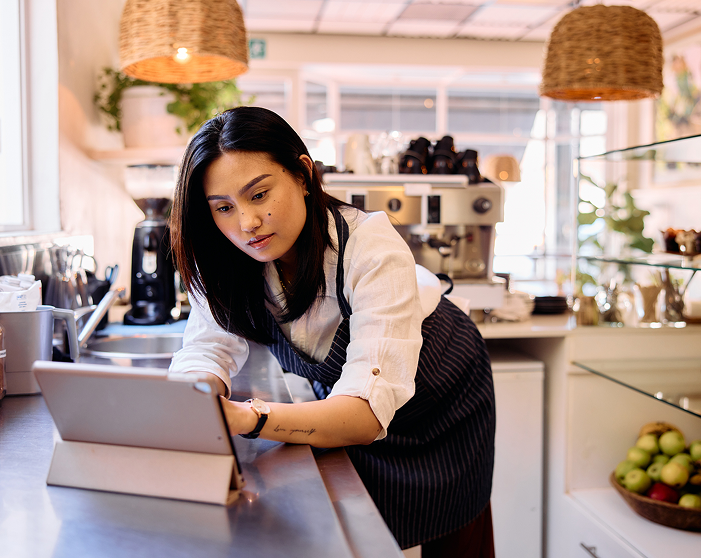 A woman with an apron using a tablet in a coffee shop